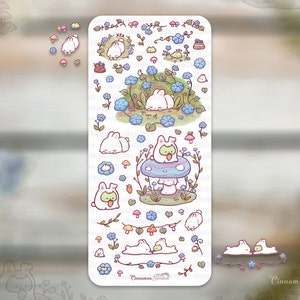 May include: A sticker sheet featuring whimsical illustrations of bunnies in a garden setting. The designs include bunnies among blue flowers, on mushrooms, and with carrots. The color palette is soft, with pastel shades of blue, pink, and green.