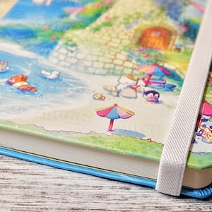 May include: A blue and white notebook with a colorful illustration of a beach scene with animals. The notebook has a white ribbon bookmark and a blue edge.