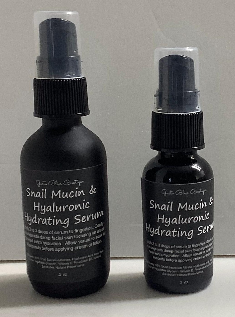 May include: Two black bottles of Snail Mucin & Hyaluronic Hydrating Serum. The larger bottle is 2 oz and the smaller bottle is 1 oz. Both bottles have a black label with white text.