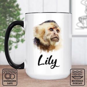May include: White ceramic mug with a black handle and rim. The mug features a watercolor image of a monkey's face and the name "Lily" in cursive. Dishwasher and microwave safe icons are also visible.