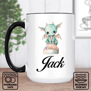 Pode incluir: Caneca de cerâmica branca com alça e borda pretas, com uma ilustração em aquarela de um dragão verde fofo com asas. O nome "Jack" está escrito em itálico abaixo. Adequado para máquina de lavar louça e micro-ondas.