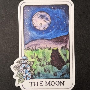May include: A tarot card illustration depicting the Moon card. The card features a full moon in a blue night sky with stars, a black wolf-like creature in the foreground, and a cluster of blue flowers in the bottom left corner. The card is titled "THE MOON".