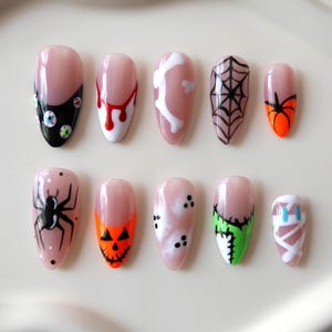 Könnte beinhalten: Ein Set aus zehn mandelförmigen Press-on-Nägeln mit verschiedenen Halloween-Motiven. Die Nägel zeigen Muster von Augäpfeln, Blutstropfen, Knochen, Spinnennetzen, Kürbissen, einer schwarzen Spinne, Geistern, grünen Nähten und einer weißen Mumienwickelung.