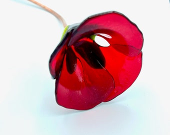 May include: A single red glass flower with a green stem. The flower has a delicate, layered design and is reminiscent of a poppy.