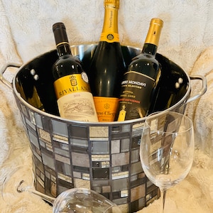 May include: A silver and black mosaic ice bucket with three bottles of wine inside. The bottles are a red wine labeled "Rivallana 2016", a champagne labeled "Veuve Clicquot Brut", and a red wine labeled "Robert Mondavi Private Selection Cabernet Sauvignon".