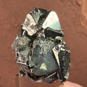 May include: A cluster of metallic pyrite crystals featuring sharp, angular, and cubic formations with a reflective, brassy gold surface. The mineral specimen displays complex geometric facets and deep, dark crevices throughout its structure.
