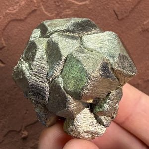 May include: A cluster of metallic pyrite crystals with a brassy gold color and cubic structure. The mineral specimen features multiple interlocking geometric faces with a reflective, shiny surface and visible striations on the crystal edges.