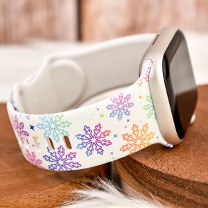 Op de afbeelding: Witte siliconen horlogeband met een regenboog sneeuwvlokkenpatroon. Het band is ontworpen voor een smartwatch.