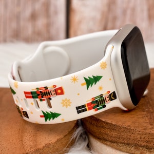 Könnte beinhalten: Weißes Silikon-Armband mit einem Weihnachts-Nussknacker- und Tannenbaum-Muster. Das Armband ist kompatibel mit Apple Watch.