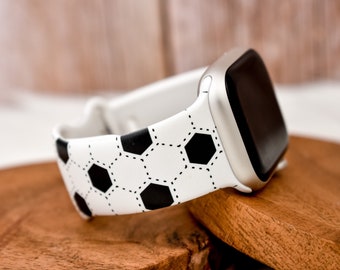 Puede incluir: Una banda de reloj Apple con estampado de balón de fútbol blanco y negro. La banda está hecha de silicona y tiene una hebilla plateada.