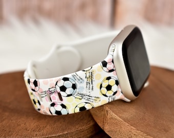 Puede incluir: Banda blanca para Apple Watch con un patrón de balón de fútbol. La banda tiene un fondo blanco con balones de fútbol y líneas de colores.