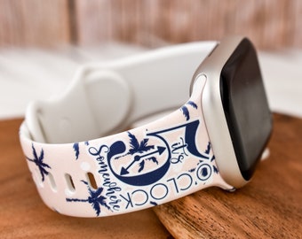 May include: A white Apple Watch band with a pink and blue tropical print. The band features palm trees and the text "It's Somewhere O'Clock".