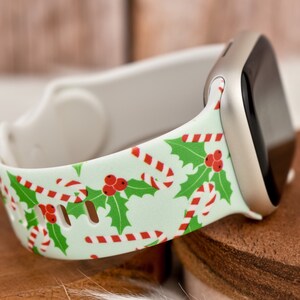 Könnte beinhalten: Ein weißes Apple Watch Armband mit einem Weihnachtsmotiv mit Zuckerstangen und Stechpalmenblättern auf hellgrünem Hintergrund.