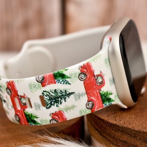 Op de afbeelding: Witte Apple Watch band met een kerstthema print met rode pick-up trucks en groene dennenbomen.