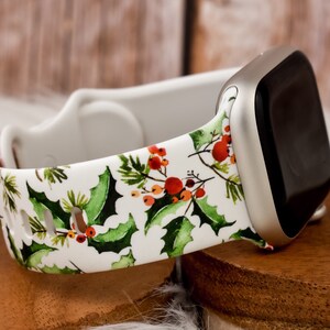 Op de afbeelding: Witte Apple Watch band met een print van hulst en bessen. De band is gemaakt van siliconen en heeft een witte achtergrond met groene hulstbladeren en rode bessen.
