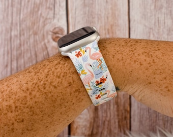 May include: A white Apple Watch band featuring a flamingo and tropical floral design. The band is worn on a person's wrist.