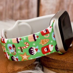 May include: A green Apple Watch band with a Christmas-themed pattern featuring gingerbread cookies, candy canes, and holiday drinks. The band is made of silicone and is compatible with Apple Watch Series 4 and later.