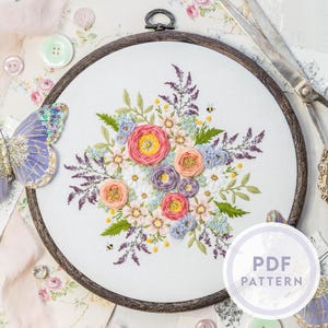 Könnte beinhalten: Blumenstickerei in einem Holzrahmen, mit einem Bouquet aus rosa, lila und gelben Blumen mit grünen Blättern und kleinen Bienen. Ein Schmetterling und eine Schere befinden sich in der Nähe des Rahmens. Das Design ist ein PDF-Muster.