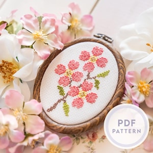 Peut inclure: Broderie au point de croix ovale de fleurs roses sur fond blanc, dans un cercle en bois. Le cercle est entouré de fleurs blanches et roses. Le texte "PDF PATTERN" est dans un cercle blanc.