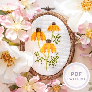 Könnte beinhalten: Eine Kreuzstichstickerei mit gelben und braunen Blumen mit grünen Stielen, in einem ovalen Holzrahmen. Die Stickerei ist von rosa und weißen Blumen umgeben. Ein weißer Kreis mit dem Text "PDF PATTERN" befindet sich unten rechts.