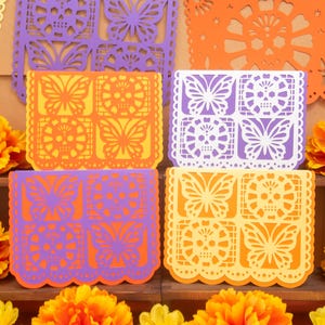 May include: A collection of rectangular paper banners featuring intricate die-cut designs of butterflies and skulls. The banners are presented in vibrant shades of purple, orange, white, and yellow, arranged in a grid pattern with scalloped edges.