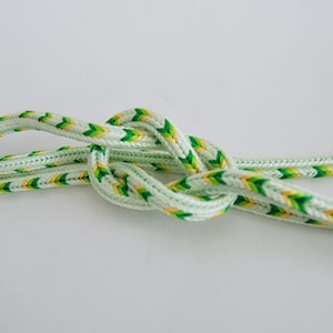 May include: A close-up of a green and yellow braided rope tied in a knot. The rope is light green with yellow and green stripes.