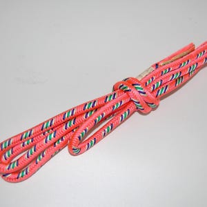 May include: A pink shoelace with green, blue and white stripes. The shoelace is tied in a knot.