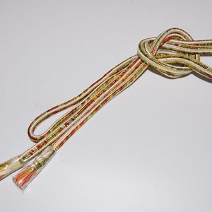 May include: A pair of white, red and green patterned cords with tassels on the ends. The cords are tied together in a knot.