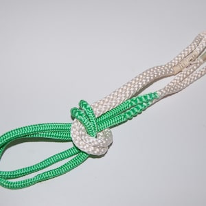 May include: A pair of green and white cords tied together in a knot. The cords are made of a thin, braided material.