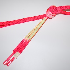 May include: Pink and white shoelaces with a herringbone pattern. The shoelaces are tied in a knot.