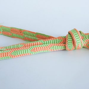 May include: A green and orange braided cord with a tassel on one end. The cord is knotted in the middle.