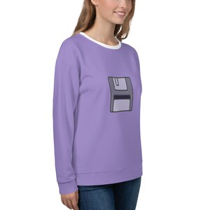 May include: A lavender sweatshirt with a white crew neck and a graphic of a gray floppy disk on the front.