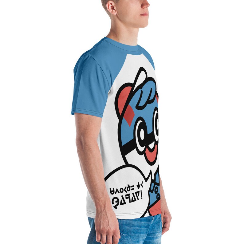 May include: White and blue raglan t-shirt featuring a cartoon character with a blue and red design. The character has a speech bubble with text in a stylized font. The sleeves are light blue.
