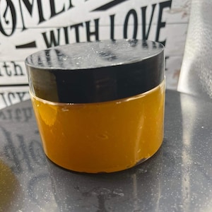 May include: A clear glass jar with a black lid filled with a bright yellow substance. The jar is sitting on a gray surface. The text "Homemade with Love" is visible in the background.