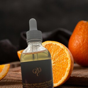 May include: A clear glass bottle with a dropper, filled with a yellow liquid, is the focal point. The bottle has a black label with gold lettering. Sliced oranges are arranged around the bottle on a wooden surface, creating a natural, fresh aesthetic.