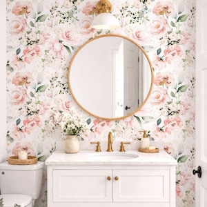 May include: A bathroom vanity with a white cabinet, marble countertop, and gold faucet, featuring a round mirror above. The wall is covered in floral wallpaper with pink roses and green leaves. A white vase with flowers sits on the counter.