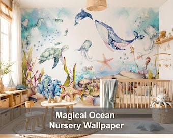 May include: A wall mural featuring a watercolour ocean scene with a large blue whale, a sea turtle, a dolphin, jellyfish, seahorses, starfish, and coral reefs. The design includes bubbles and aquatic plants in shades of blue, green, and pink on a white background, covering the entire wall behind a wooden crib.