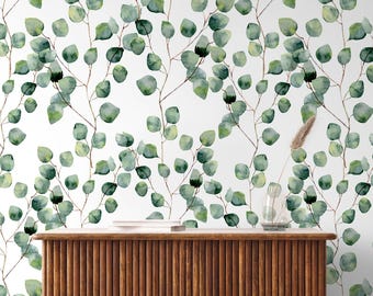 May include: A wallpaper featuring a repeating watercolor pattern of green eucalyptus leaves on thin brown stems against a white background. Below the wallpaper sits a wooden console table with a slatted front, two books, and a glass vase.