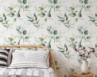 May include: Wallpaper featuring a repeating watercolor pattern of green eucalyptus leaves and branches on a white background, positioned behind a bed with striped bedding and a rattan side table holding a vase with dried cotton stems.