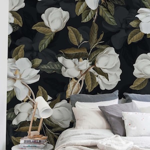 May include: Dark floral wallpaper with large white magnolia flowers and green and brown leaves. The flowers are set against a dark background, creating a dramatic contrast. The wallpaper is installed in a bedroom setting.