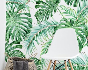 May include: A white chair with wooden legs sits in front of a wall covered in wallpaper featuring a pattern of large green monstera leaves and palm fronds. A woven basket with a dark gray cloth draped over the side is positioned nearby.