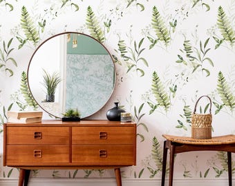 May include: A wooden dresser with four drawers sits against a wall covered in white wallpaper featuring a green fern and botanical leaf pattern. A round mirror, a black vase, a small woven basket, and a pair of beige sandals are visible.