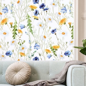 Può includere: Carta da parati con un motivo botanico di margherite bianche, denti di leone gialli e campanule blu su sfondo bianco. Il design include steli e foglie verdi, creando un aspetto simile a un prato sulla superficie della parete.