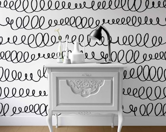 May include: A white nightstand with a single drawer featuring ornate carved detailing, positioned against a wall covered in wallpaper with a repeating black hand-drawn scribble pattern. A black desk lamp and a white vase sit on top.