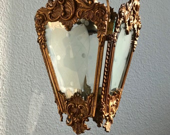 May include: A gold-toned ornate metal chandelier with a clear glass shade. The chandelier has a decorative design with intricate details.