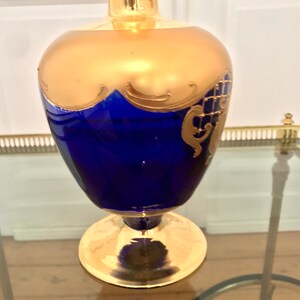 May include: A cobalt blue glass vase with gold accents and intricate designs. The vase has a wide base and a narrow neck.