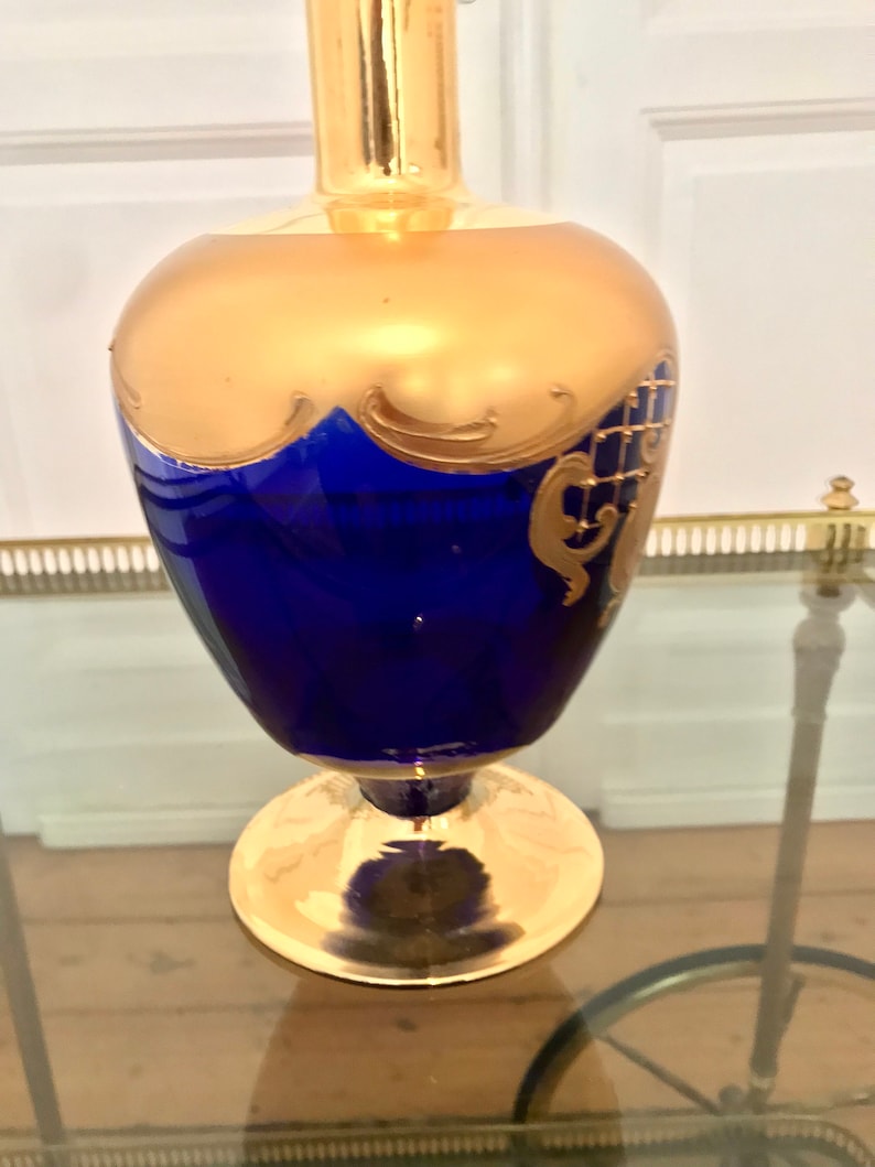 May include: A cobalt blue glass vase with gold accents and intricate designs. The vase has a wide base and a narrow neck.