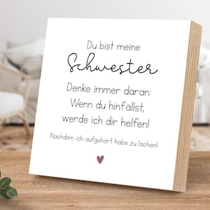 Peut inclure: Une pancarte en bois blanc avec du texte noir qui dit "Du bist meine Schwester. Denke immer daran: Wenn du hinfällst, werde ich dir helfen! Nachdem ich aufgehört habe zu lachen!" avec un petit cœur rose en bas.