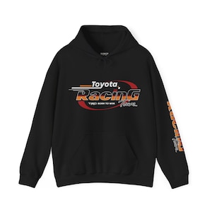 May include: A black hooded sweatshirt featuring a graphic on the chest that reads Toyota Racing Team with the text TRD BORN TO WIN. The design includes red, orange, and white accents. The word Racing Team is also printed vertically on the left sleeve.