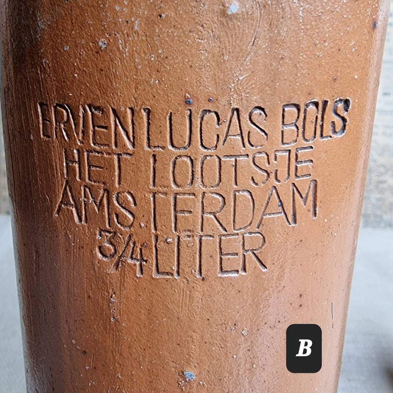 K&ouml;nnte beinhalten: Eine braune Keramikkanne mit der Aufschrift "ERVEN LUCAS BOLS HET LOOTSJE AMSTERDAM 3/4 LITER" in wei&szlig;er Schrift.